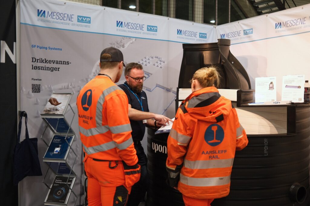 En utstiller på VA messene demonstrer et produkt for to besøkende på messen